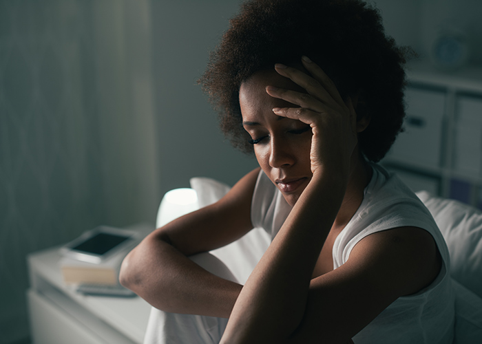 Woman in a darkened room holding her head to indicate a migraine